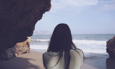 女人坐在岩石面临大海
